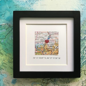 May include: A framed map with a red heart marking a location in the Atlanta, Georgia area. The coordinates 34° 13' 38.89" N, 84° 27' 37.58" W are printed below the map.