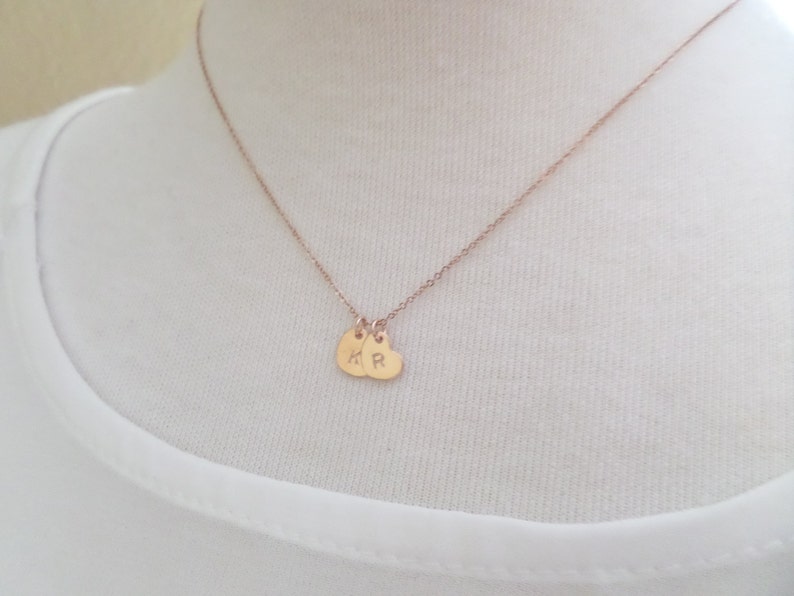 Puede incluir: Un collar de oro rosa con dos peque&ntilde;os colgantes en forma de coraz&oacute;n. Los colgantes est&aacute;n grabados con las letras "K" y "R".