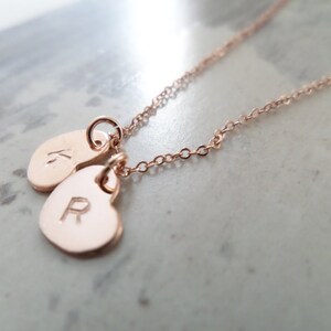 Puede incluir: Un collar de oro rosa con dos colgantes en forma de coraz&oacute;n. Los colgantes est&aacute;n grabados con las letras "K" y "R".