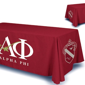 May include: Red table cover with white Alpha Phi logo and crest. The logo features a vine with leaves and the letters "A" and "Phi" intertwined. The crest is a shield with a bird and a banner.