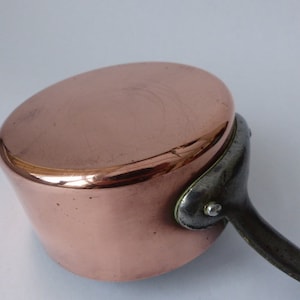 Puede incluir: Una cacerola de cobre con un mango de metal negro. La cacerola tiene un acabado de cobre brillante y un fondo redondeado.