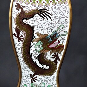K&ouml;nnte beinhalten: Ein wei&szlig;es Emaille-Objekt mit einer detaillierten Darstellung eines gr&uuml;nen, braunen und roten Drachen auf wei&szlig;em Hintergrund mit einem Muster aus wei&szlig;en Wolken. Der Drache hat ein blaues Auge und einen rosa Mund.