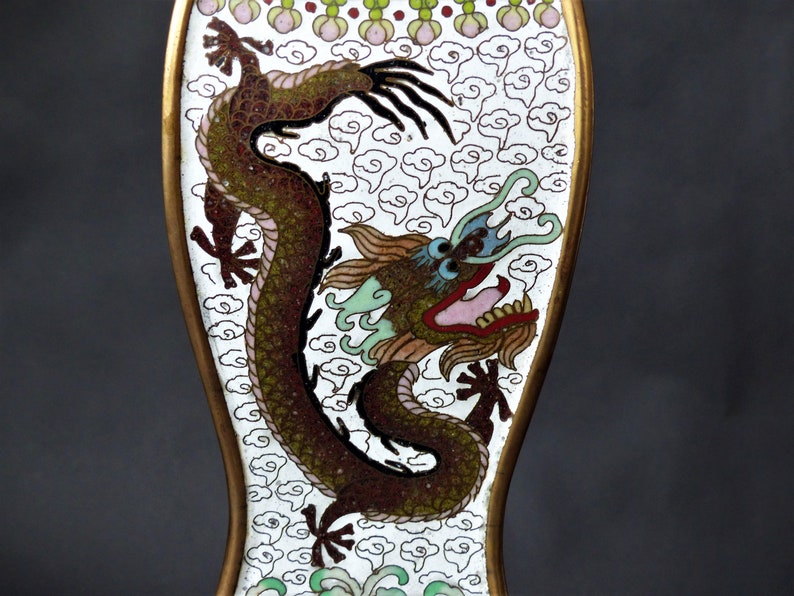K&ouml;nnte beinhalten: Ein wei&szlig;es Emaille-Objekt mit einer detaillierten Darstellung eines gr&uuml;nen, braunen und roten Drachen auf wei&szlig;em Hintergrund mit einem Muster aus wei&szlig;en Wolken. Der Drache hat ein blaues Auge und einen rosa Mund.