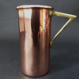May include: A copper mug with a brass handle. The mug is cylindrical and has a smooth, polished surface.