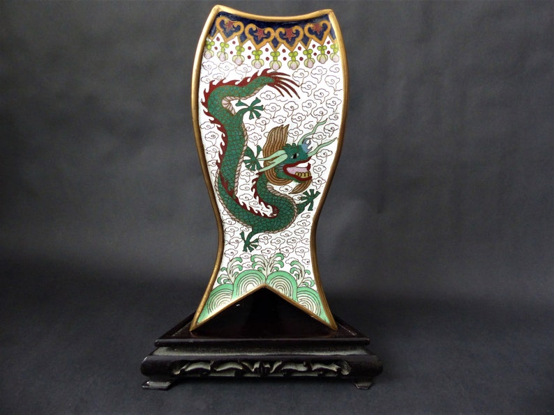 K&ouml;nnte beinhalten: Ein wei&szlig;es und goldenes Cloisonn&eacute;-Emaille-Dekorationsst&uuml;ck mit einem gr&uuml;nen Drachenmotiv auf einem schwarzen Holzsockel.