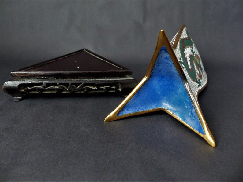 K&ouml;nnte beinhalten: Ein dreieckiger Holzst&auml;nder mit aufwendigen Schnitzereien und einer blauen und wei&szlig;en Emaille-Drachenfigur darauf. Die Drachenfigur hat goldene Akzente und einen wei&szlig;en Hintergrund mit gr&uuml;nen und roten Details.