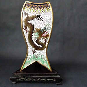 K&ouml;nnte beinhalten: Eine wei&szlig;e und goldene Cloisonn&eacute;-Vase mit einem Drachenmotiv. Die Vase steht auf einem schwarzen Holzsockel.