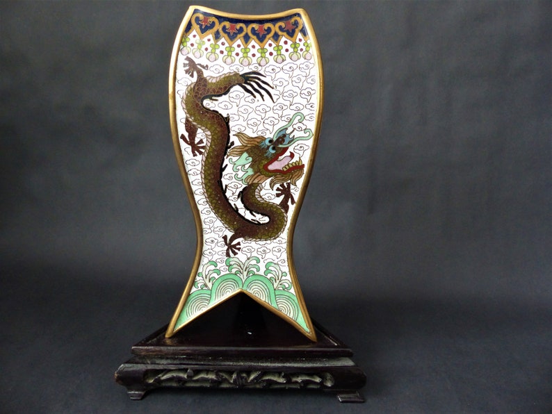 K&ouml;nnte beinhalten: Eine wei&szlig;e und goldene Cloisonn&eacute;-Vase mit einem Drachenmotiv. Die Vase steht auf einem schwarzen Holzsockel.