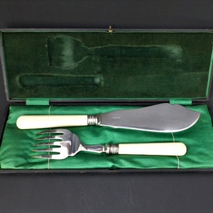 Puede incluir: Un cuchillo de mantequilla de plata y un tenedor de plata con mangos de marfil se muestran en una caja forrada de terciopelo verde.