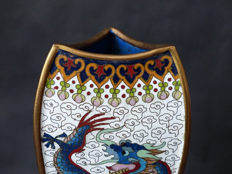K&ouml;nnte beinhalten: Eine wei&szlig;e Keramikvase mit einem blauen und roten Drachenmuster. Die Vase hat einen goldenen Rand und ein dekoratives Muster um die Oberseite.