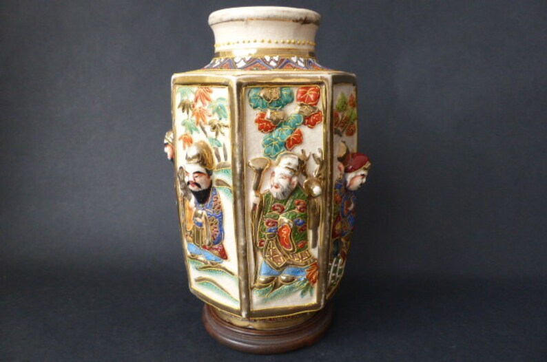 Może przedstawiać: Sześciokątny wazon z porcelany z pozłacanym wykończeniem i misternymi ręcznie malowanymi detalami. Wazon przedstawia scenę z postaciami w tradycyjnych japońskich strojach, otoczonymi kwiatami i liśćmi.