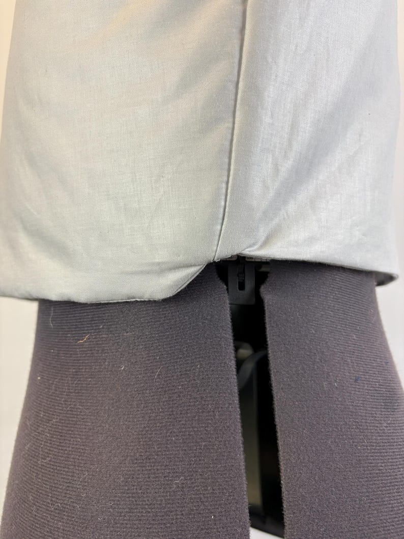 May include: Close-up of a light gray fabric garment. The fabric appears to be a lightweight material, possibly linen or cotton, with a subtle texture. The garment is sewn with a visible seam. The garment is placed on a black dress form.