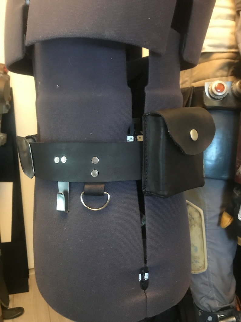 May include: A black leather belt with a silver buckle and a small black leather pouch attached to it. The belt is worn on a gray mannequin.