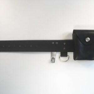 May include: A black leather belt with a small black leather pouch attached. The belt has multiple silver metal eyelets and a silver metal buckle. The pouch has a silver metal button.