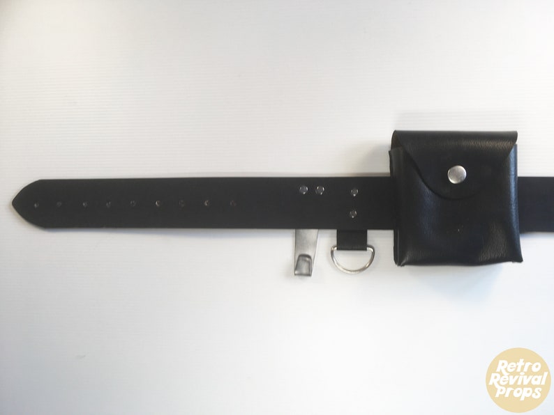 May include: A black leather belt with a small black leather pouch attached. The belt has multiple silver metal eyelets and a silver metal buckle. The pouch has a silver metal button.