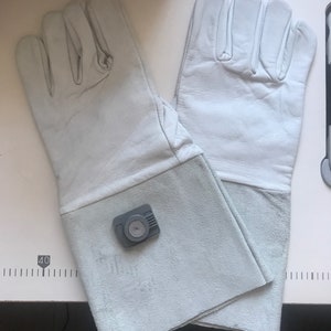May include: A pair of light blue leather work gloves with a gray safety device attached to the cuff of one glove.