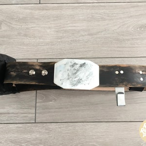 May include: A black leather belt with a silver buckle and a white marble-like design. The belt has a small black pouch attached to it.