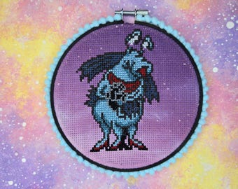 May include: A blue and purple cross-stitch embroidery hoop with a cartoon monster holding a microphone. The monster has a purple body, black hair, and red shoes. The background is a gradient of purple and pink.