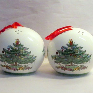 May include: A pair of white ceramic Christmas tree salt and pepper shakers with red ribbon accents. The shakers are decorated with a green Christmas tree with ornaments and presents.