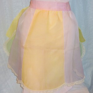 May include: A pastel-colored sheer apron with a pink waistband and white lace trim. The apron is made of a lightweight fabric and has a scalloped hem.