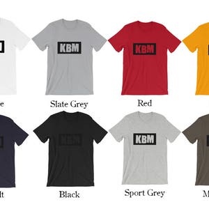 May include: A mockup of a t-shirt with the text "KBM" in a black box on the front. The t-shirt is shown in ten different colors: white, slate grey, red, gold, asphalt, black, sport grey, military, navy, and heather grey.