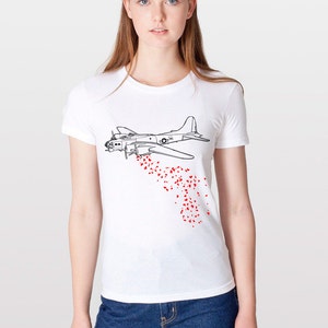 Puede incluir: Una camiseta blanca con un dibujo en línea negra de un bombardero B-17 que deja caer corazones rojos.