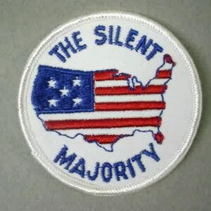 Puede incluir: Un parche bordado blanco con un contorno azul. El parche presenta una bandera estadounidense roja, blanca y azul en forma de los Estados Unidos. El texto "The Silent Majority" está escrito en azul alrededor de la bandera.