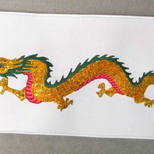 May include: A white fabric patch with an embroidered gold dragon with green accents and a pink underbelly. The dragon is facing right and has a long, curled tail.