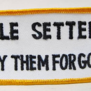 May include: A white embroidered patch with a yellow border. The patch reads "TILE SETTERS LAY THEM FOR GOOD".