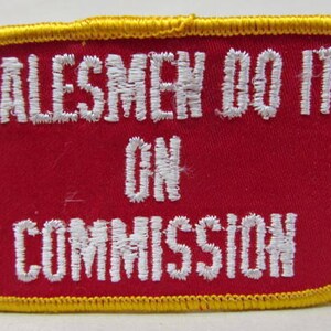 Puede incluir: Parche rojo bordado con costuras amarillas alrededor de los bordes. El parche dice "Salesmen Do It On Commission" en letras blancas.