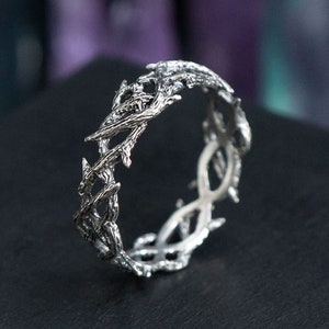 May include: A silver ring with a detailed design of intertwined branches, resembling a crown of thorns.