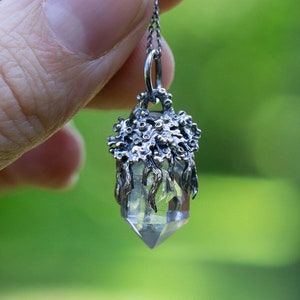 May include: A silver pendant necklace featuring a clear quartz crystal encased in a detailed, silver, tree-like design.