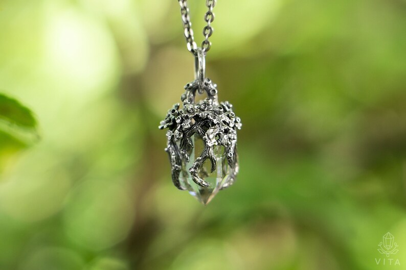 May include: A silver necklace with a clear crystal pendant encased in a delicate silver tree branch design.