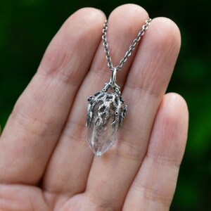 May include: A silver necklace with a clear quartz crystal pendant encased in a silver, tree-like design.