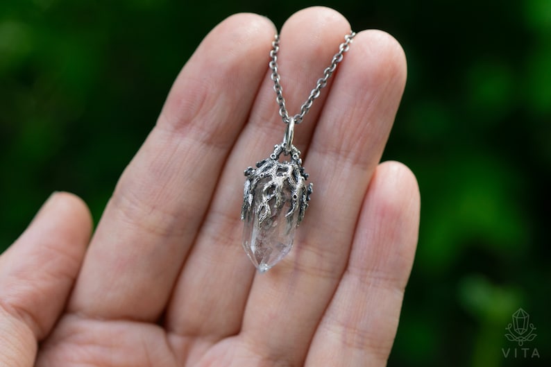 May include: A silver necklace with a clear quartz crystal pendant encased in a silver, tree-like design.