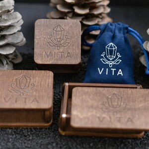 May include: Four wooden boxes with the word "VITA" engraved on them. The boxes are arranged in a square shape. A blue velvet bag with the word "VITA" engraved on it is in the center of the square.