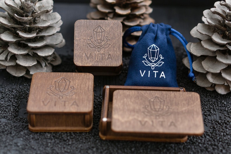May include: Four wooden boxes with the word "VITA" engraved on them. The boxes are arranged in a square shape. A blue velvet bag with the word "VITA" engraved on it is in the center of the square.