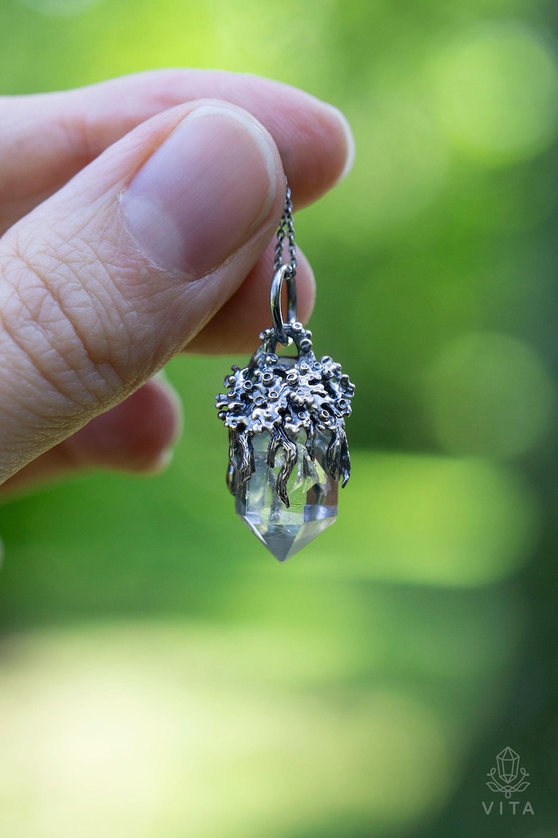 May include: A silver pendant necklace featuring a clear quartz crystal encased in a detailed, silver, tree-like design.