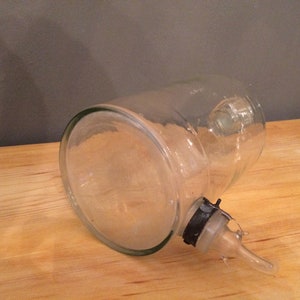 May include: A clear glass bottle with a spout and a black plastic cap. The bottle is lying on its side on a wooden surface.