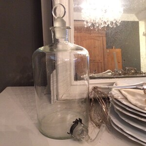 May include: A clear glass bottle with a stopper and a spout. The bottle is sitting on a white surface.