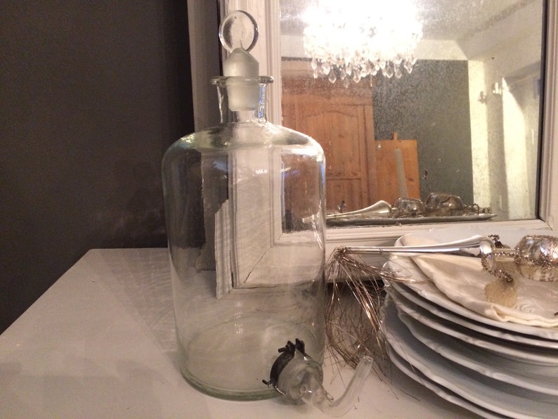 May include: A clear glass bottle with a stopper and a spout. The bottle is sitting on a white surface.