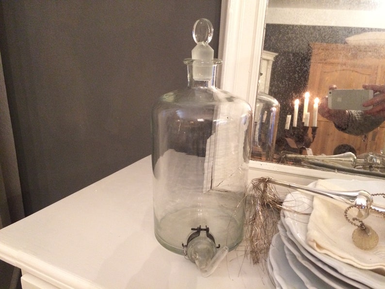 May include: A clear glass bottle with a glass stopper and a spout. The bottle is sitting on a white surface.