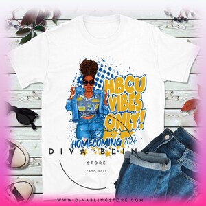 May include: White t-shirt featuring a graphic of a Black woman wearing a denim jacket and jeans. The graphic includes the text "HBCU Vibes Only! Homecoming 2024" and a blue and white polka dot background. The text "DivaBling Store Est 2013" is at the bottom of the shirt.