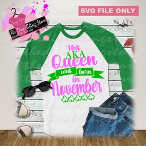 May include: A white and green baseball style t-shirt with the text "This AKA Queen was born in November" in pink and green lettering. There are five green stars below the text.