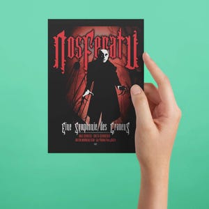 May include: A black and red poster with the title "Nosferatu" and the text "Eine Symphonie des Grauens". The poster features a black and white image of a man in a long coat with a pale face and dark eyes.