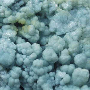 May include: Close-up of a mineral formation with a bubbly, clustered structure. The mineral has a pale blue-green color, with some areas appearing more opaque and others translucent. The overall texture is rough and uneven, with a crystalline appearance.