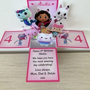 May include: A pink and white pop-up card with a 4 on each side. The card features a girl with brown hair and a pink shirt, and several cartoon cats. The card reads "Happy 4th Birthday Alaska. We hope you have the most amazing day celebrating! Love always, Mum, Dad & Shiloh XOXO".