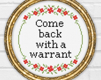 May include: A gold framed embroidery hoop with a white background and green and red floral border. The text "Come back with a warrant" is stitched in black thread.