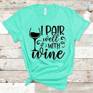 May include: A turquoise blue t-shirt with a black graphic of a wine glass and the text "I pair well with wine".