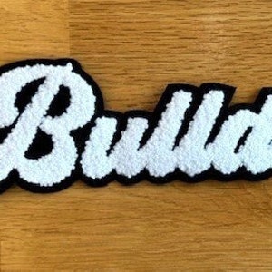 May include: White felt "Bulldogs" lettering with black outline. The letters are in a cursive font.